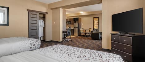 Habitación de hotel con dos camas, televisión, escritorio y kitchenette.
