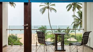 A balcony with a view of the beach, two chairs, and a table.