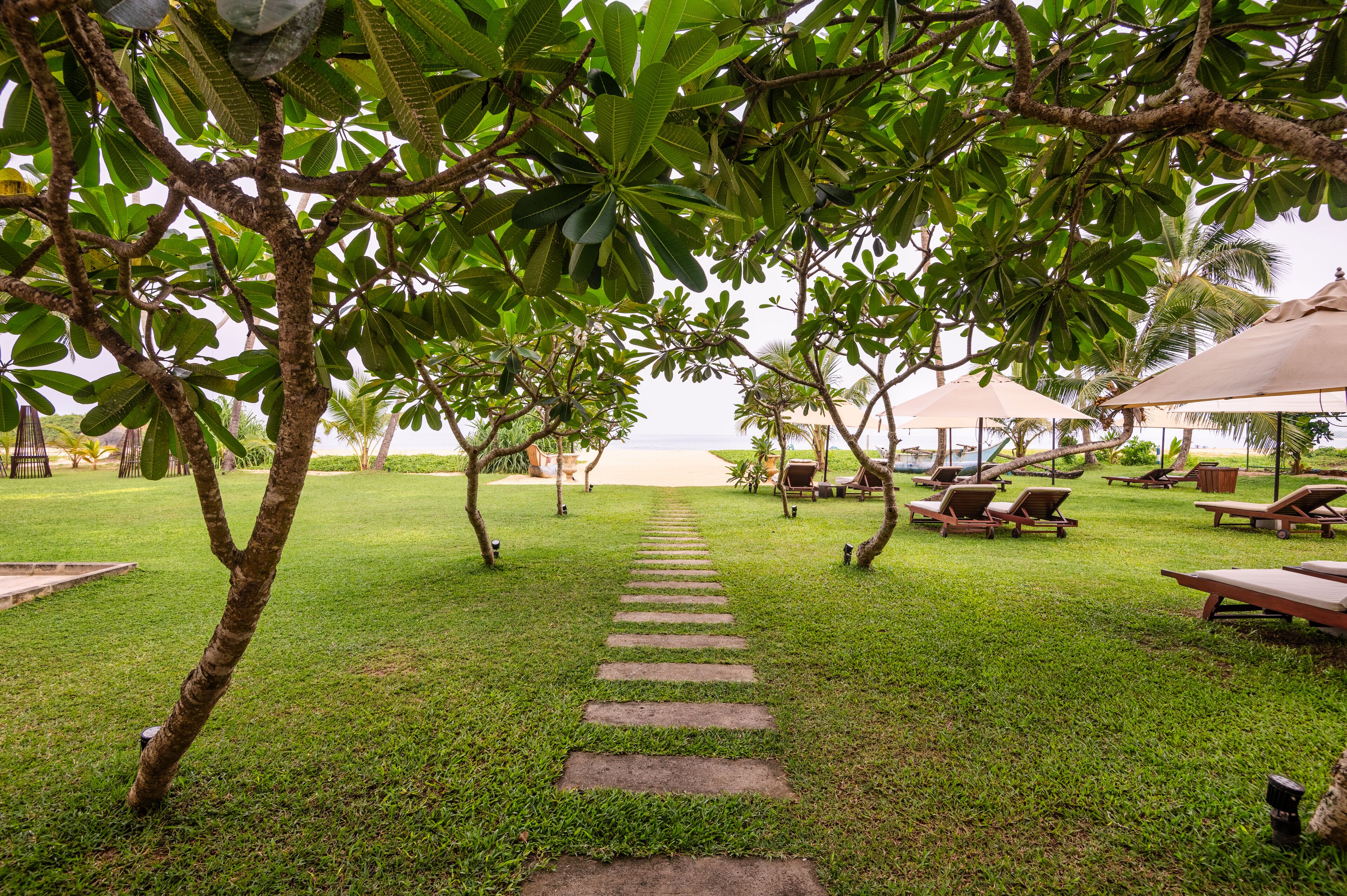 Un sendero que lleva a una zona de playa con sillas de descanso y sombrillas.