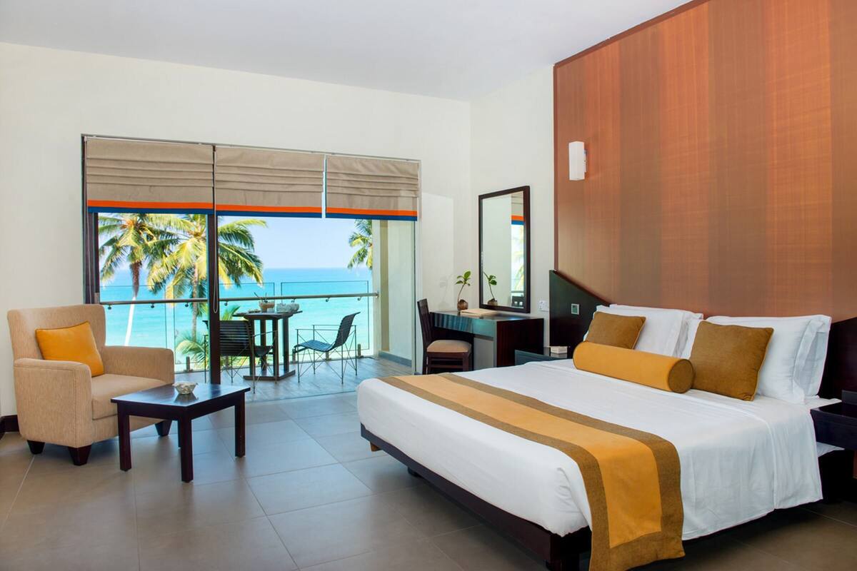 A hotel room with a bed, a desk, a chair, and a view of the ocean.