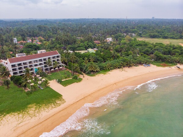 An aerial view of a coastal hotel with multiple floors, surrounded by lush greenery and a sandy beach. - Shinagawa Beach (Balapitiya)