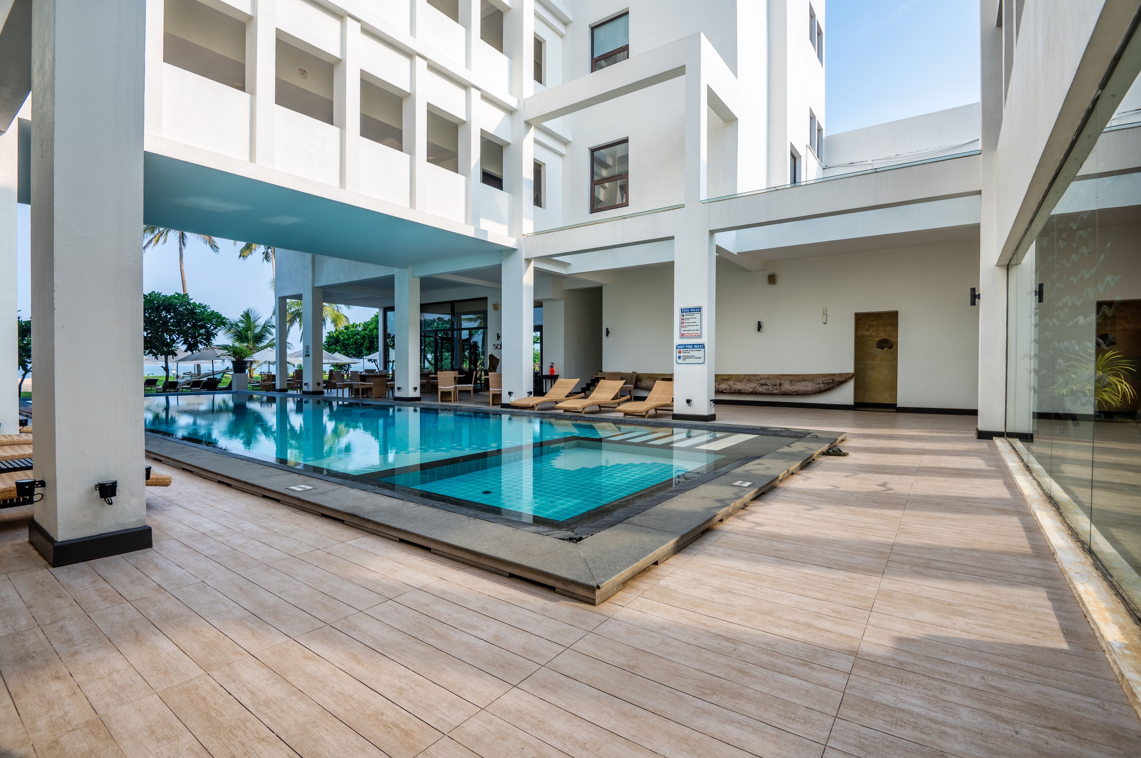 A modern indoor swimming pool with clear blue water, surrounded by wooden deck and lounge chairs.