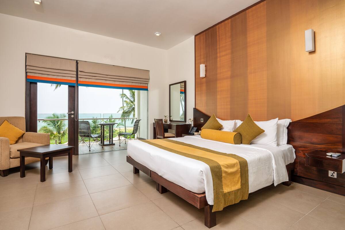 A hotel room with a large bed, a sofa, a desk, and a balcony with a view.
