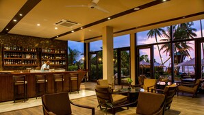 A bar area with a bartender, wooden furniture, and a view of palm trees through large windows. - Shinagawa Beach (Balapitiya)