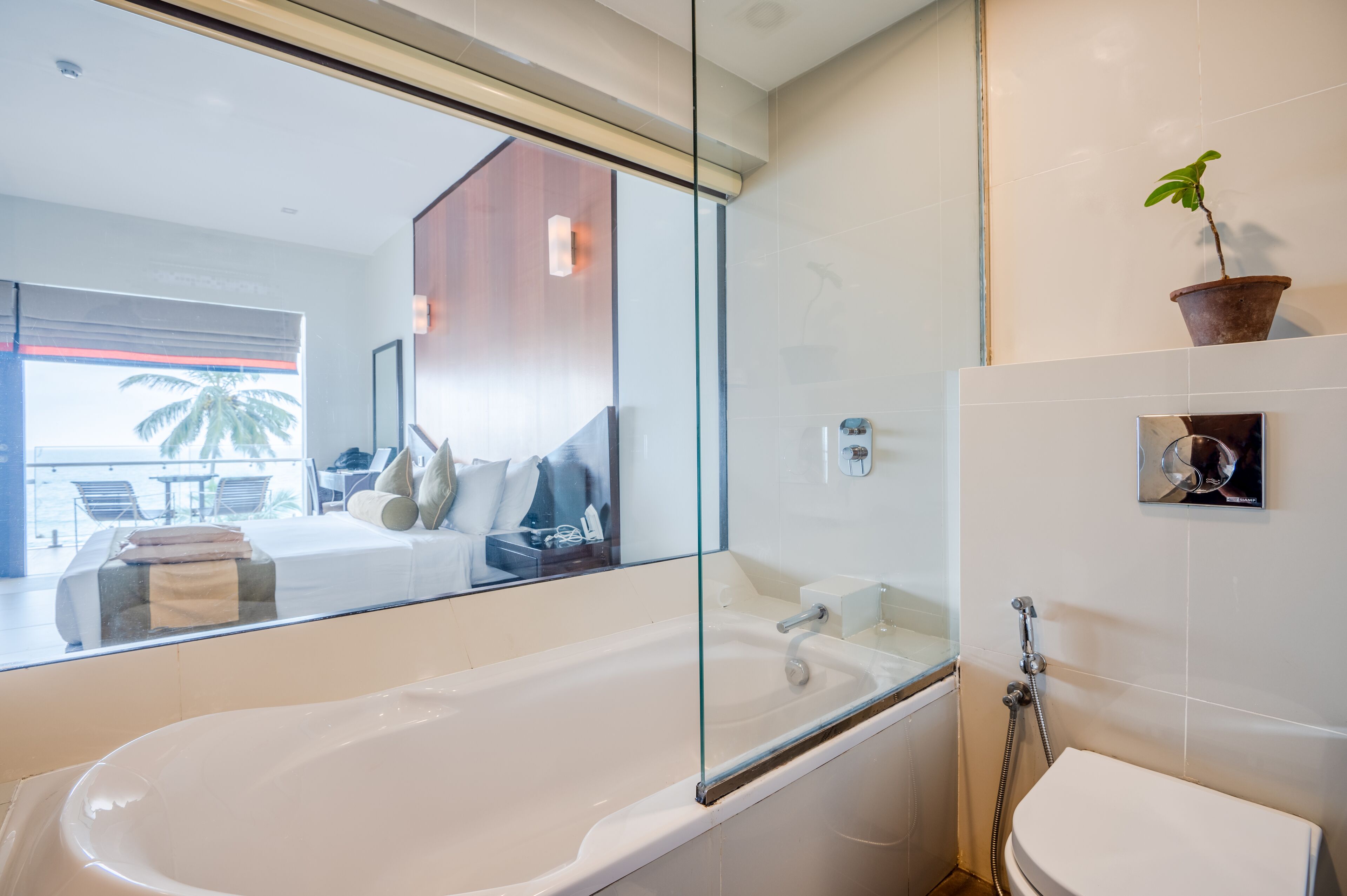 Un baño moderno con una bañera grande, un inodoro y una ducha. Hay un espejo grande sobre la bañera y una planta en maceta en la pared.