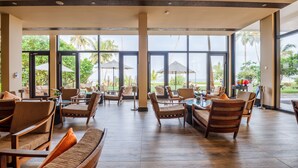 A spacious indoor area with large windows, wicker furniture, and a view of palm trees and a beach. - Shinagawa Beach (Balapitiya)