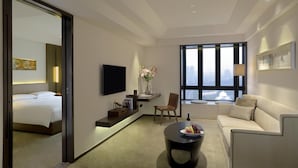 Ein modernes Hotelzimmer mit Bett, einer Sitzecke, einem Fernseher, einem Couchtisch und einem großen Fenster mit Blick auf die Stadt.