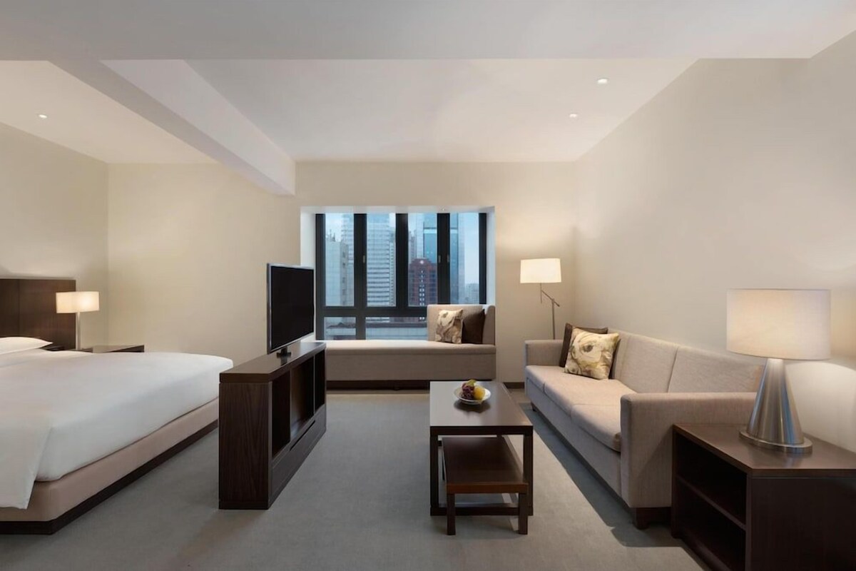 Ein Hotelzimmer mit Bett, Fernseher, Sofa, Couchtisch und Fenster mit Stadtblick.