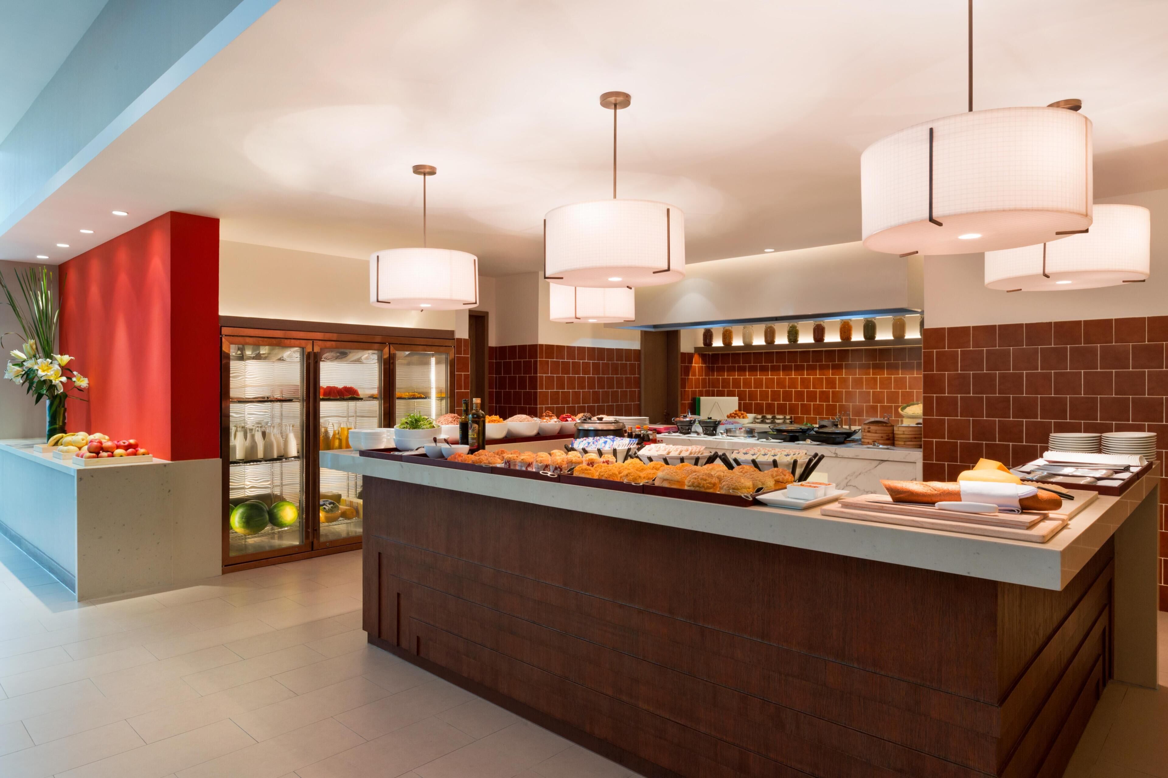 A modern kitchen with a central island, pendant lighting, and a glass-fronted refrigerator.