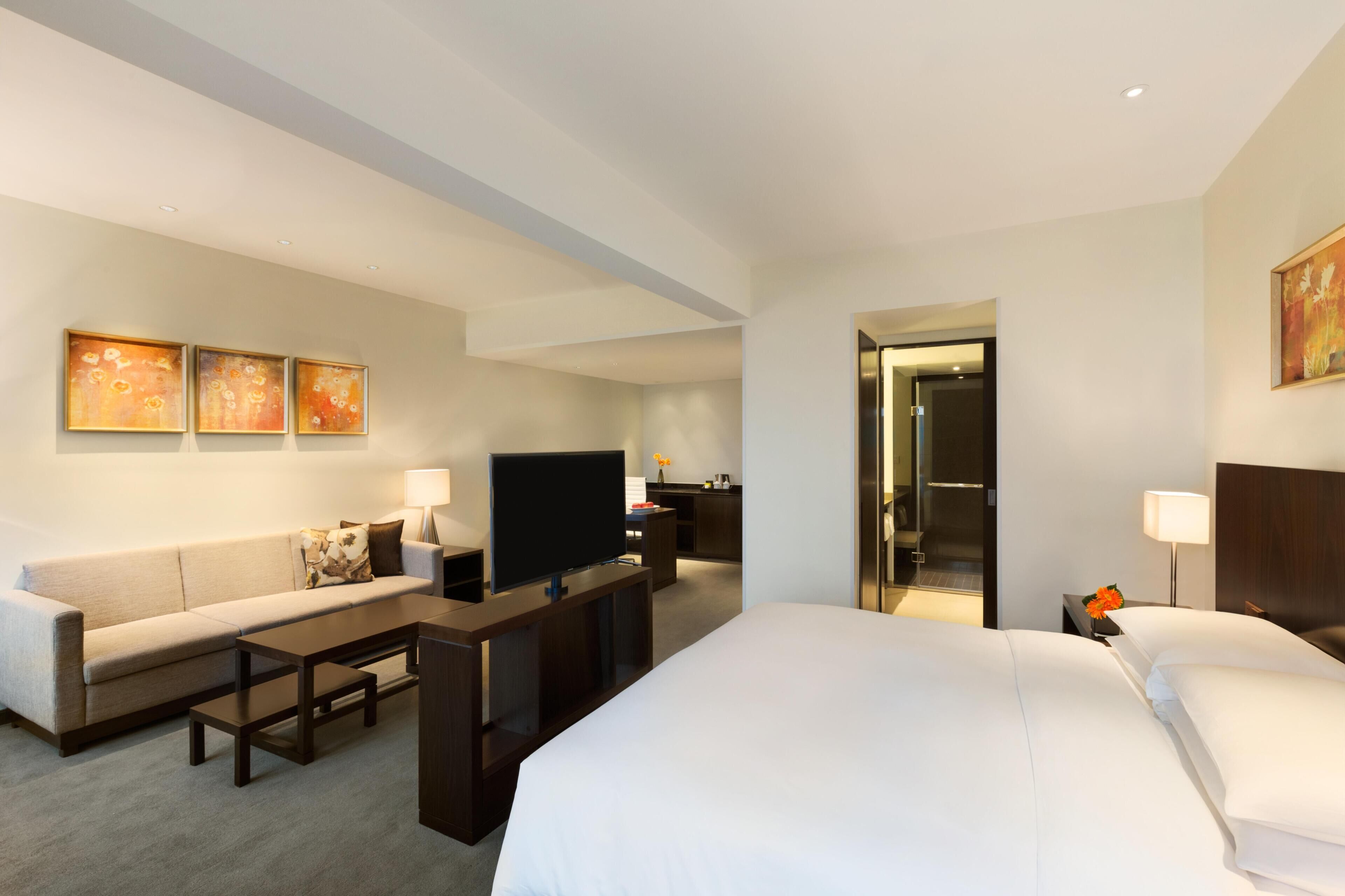 Ein Hotelzimmer mit Bett, Sofa, Fernseher, Schreibtisch und Bad.