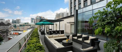 Un salón en la azotea con asientos exteriores, una sombrilla verde y vistas de la ciudad.
