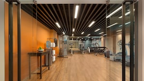 Ein modernes Fitnessstudio mit Trainingsgeräten, Holzboden und einer Glassturzwand.
