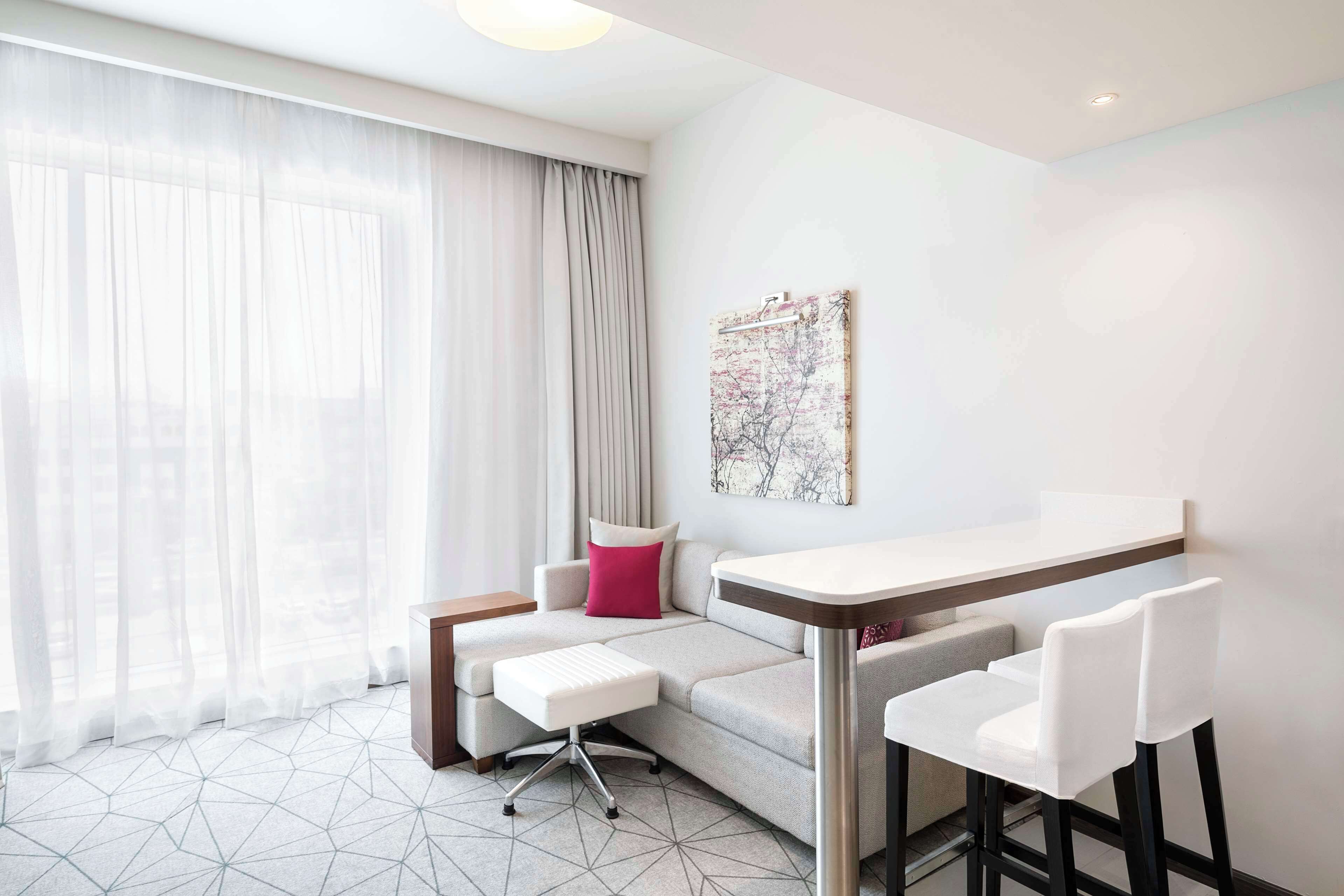 A modern hotel room with a sofa, a small table, and a bar area.