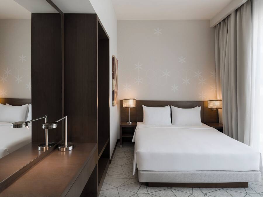 A hotel room with a large bed, two bedside tables with lamps, a mirror, and a geometric-patterned wall.