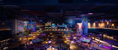 A spacious restaurant with multiple tables and chairs, a bar area, and a stage for performances.