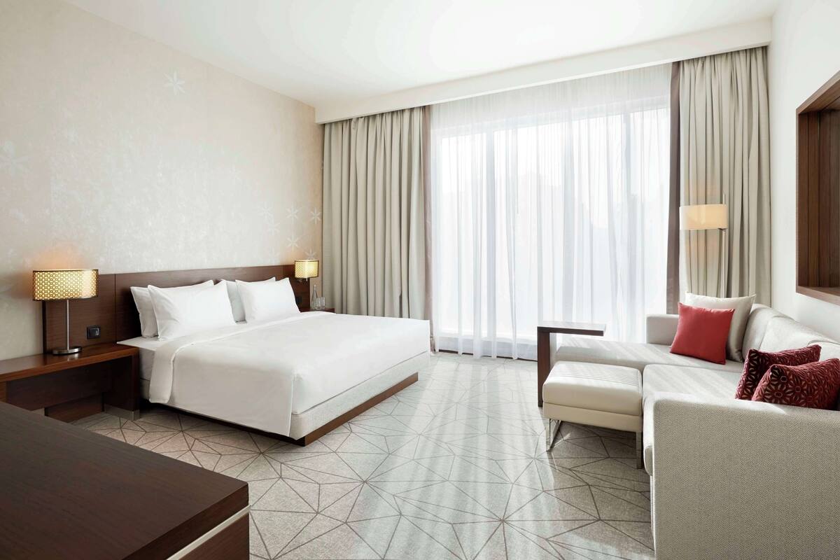 A hotel room with a large bed, a sofa, a desk, and a window with curtains.