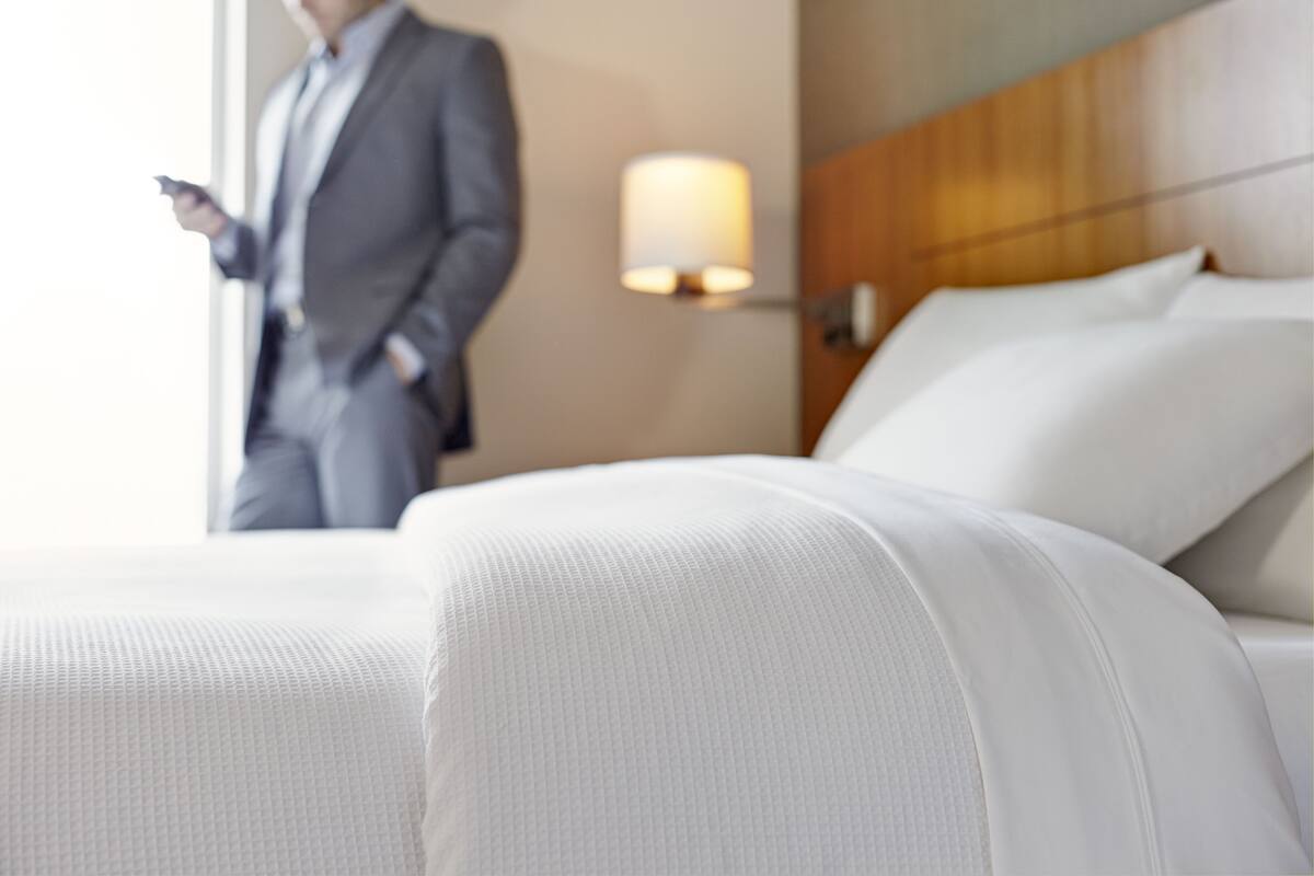 A hotel room with a bed, a nightstand, and a lamp.