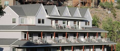 Un hotel de varios pisos con balcones, un porche cubierto y un paisaje montañoso al fondo.
