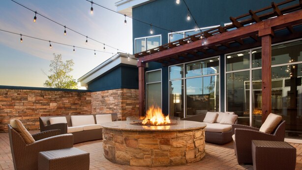 Un patio al aire libre con un hogar de piedra, mobiliario de mimbre e iluminación con luces colgantes.
