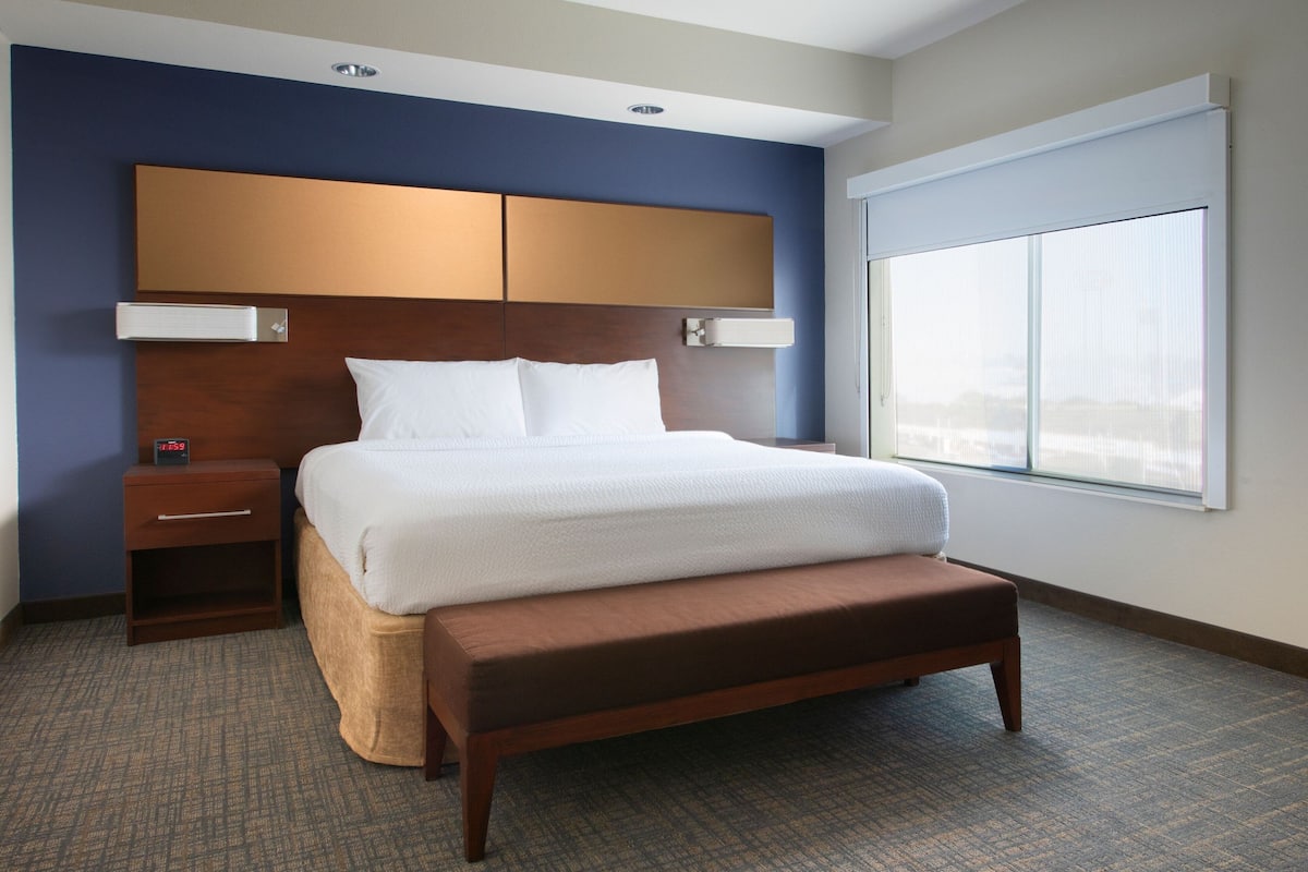A hotel room with a large bed, a wooden headboard, a nightstand, and a window with a view.
