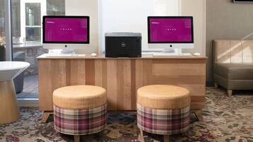 A room with two monitors on a wooden desk, a printer, and two plaid stools.