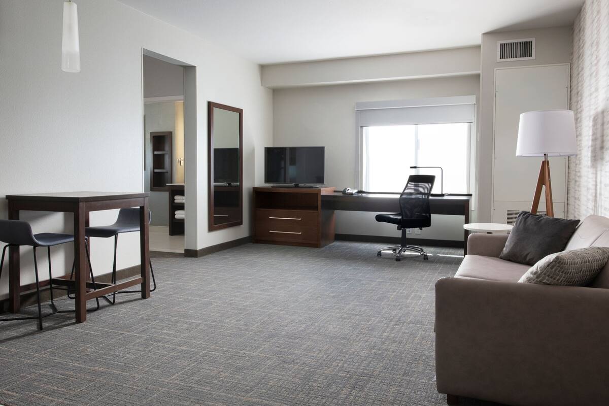 A hotel room with a desk, two chairs, a sofa, a TV, and a window.