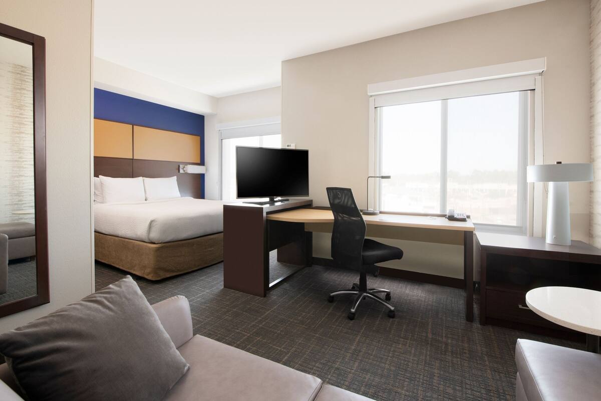 A hotel room with a bed, a desk, a chair, a TV, a lamp, and a window.