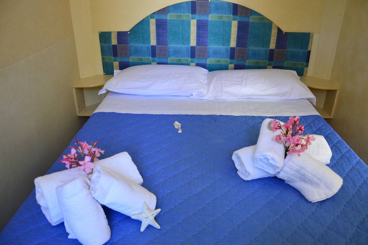 A bed with a blue quilt, white pillows, and two towels with flowers and a starfish.
