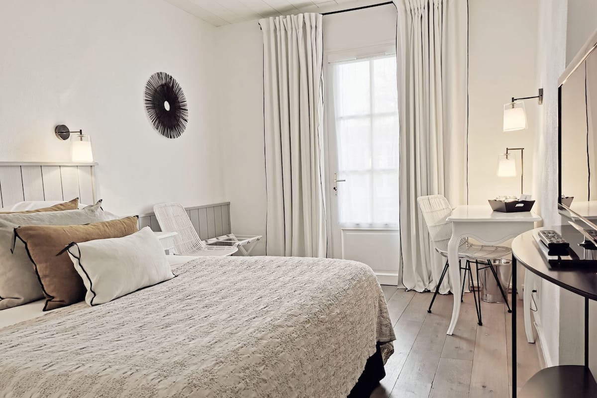A bedroom with a large bed, a desk, a chair, and a window with curtains.