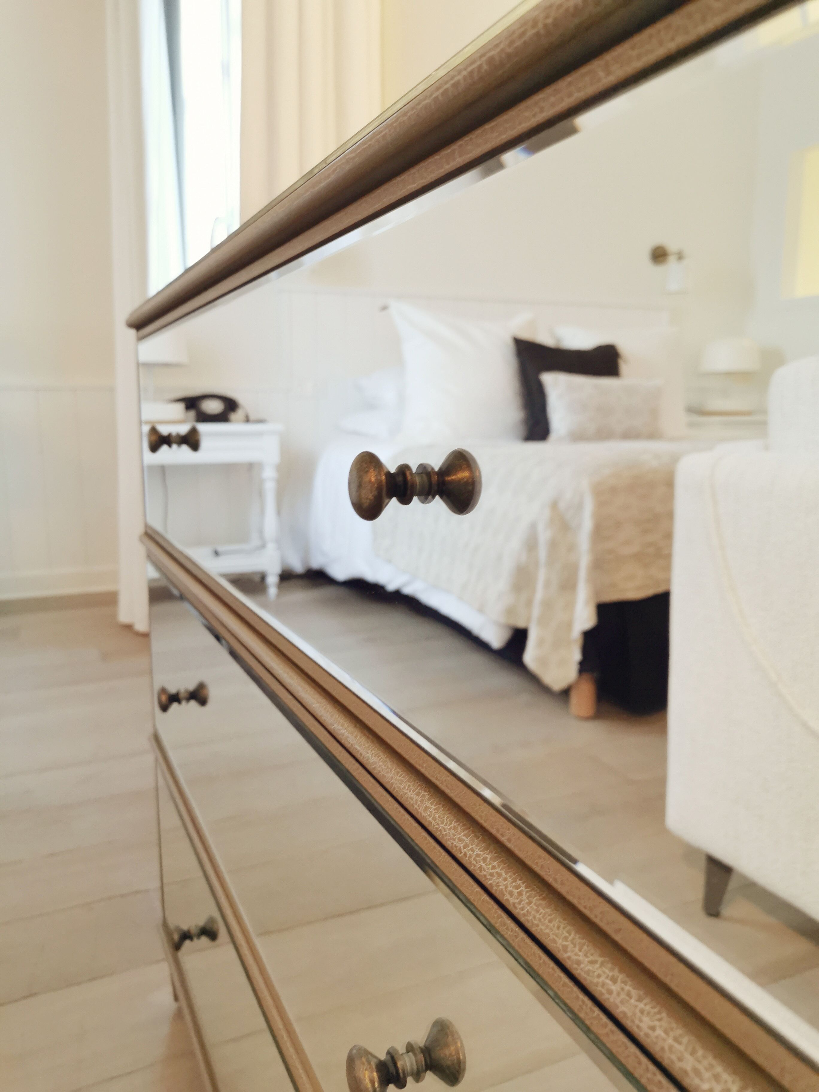 Un dormitorio con un espejo grande que refleja una cama, una mesita de noche y un tocador.