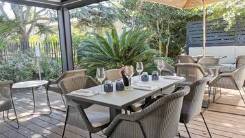Un patio al aire libre con mobiliario de mimbre, una mesa dispuesta para comer y un gran paraguas que da sombra.