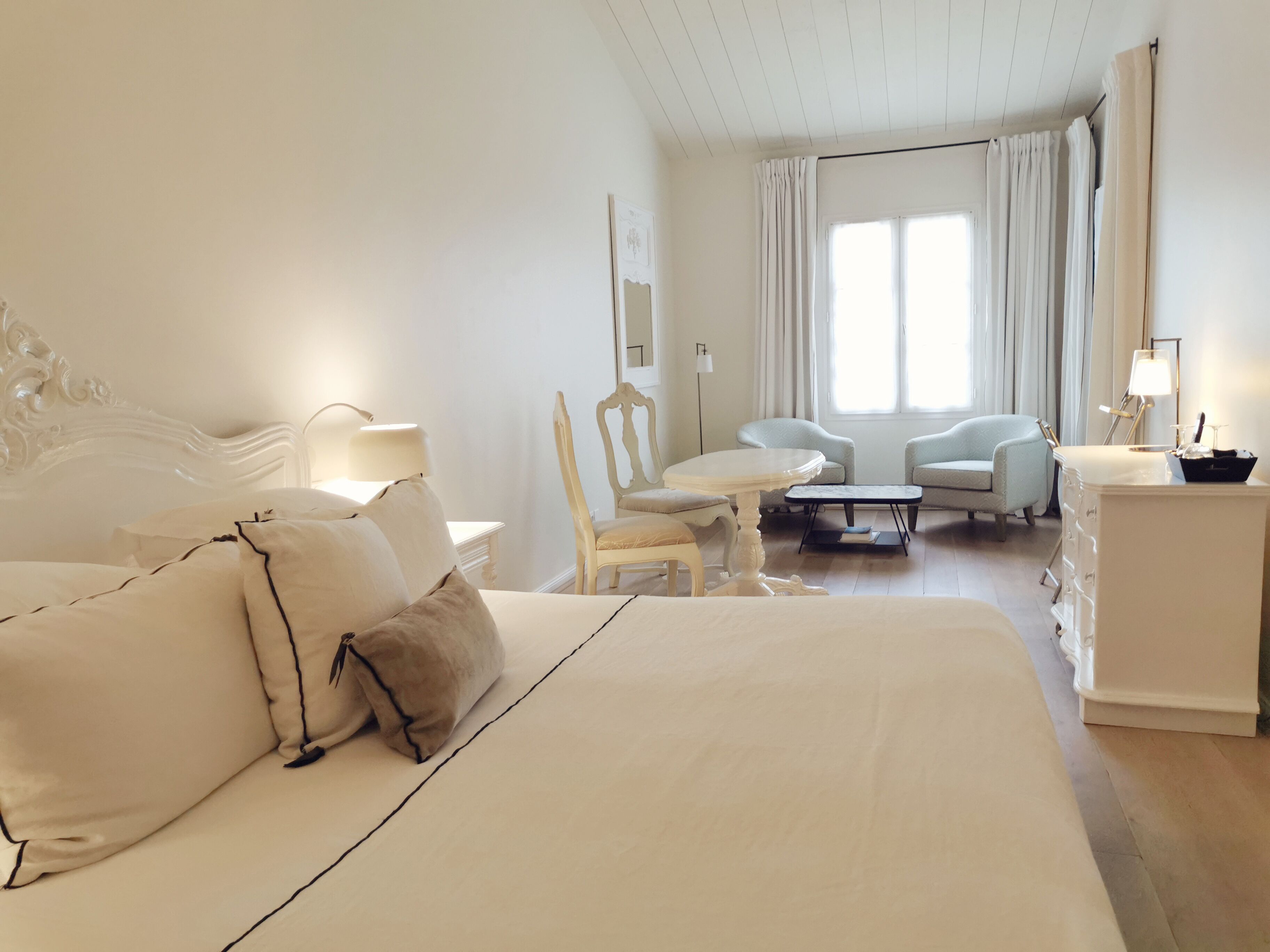 Een hotelkamer met een groot bed, een zithoek met twee stoelen, een kleine tafel en een dressoir met lades.