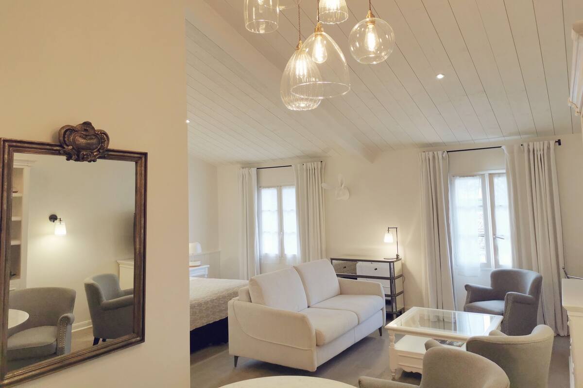 A spacious living room with a white sofa, armchairs, a glass coffee table, and a large mirror.