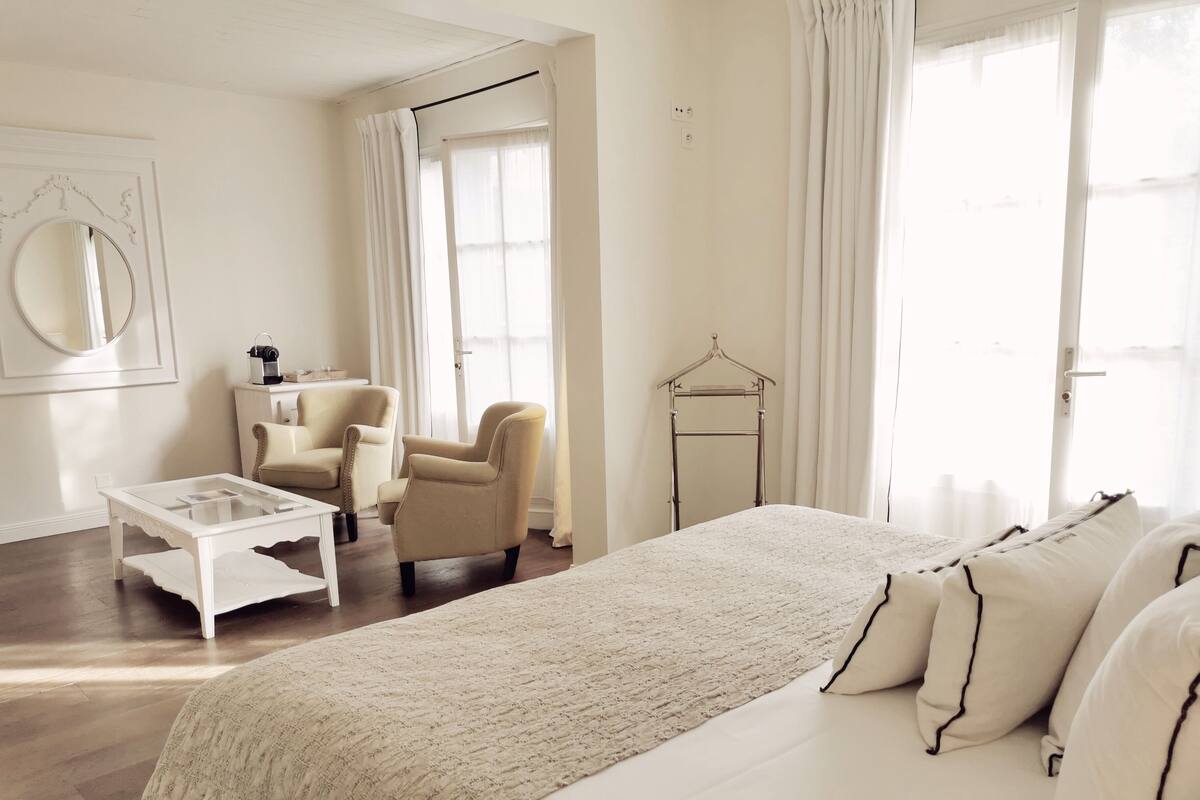 A bedroom with a large bed, a chair, a small table, and a wardrobe.