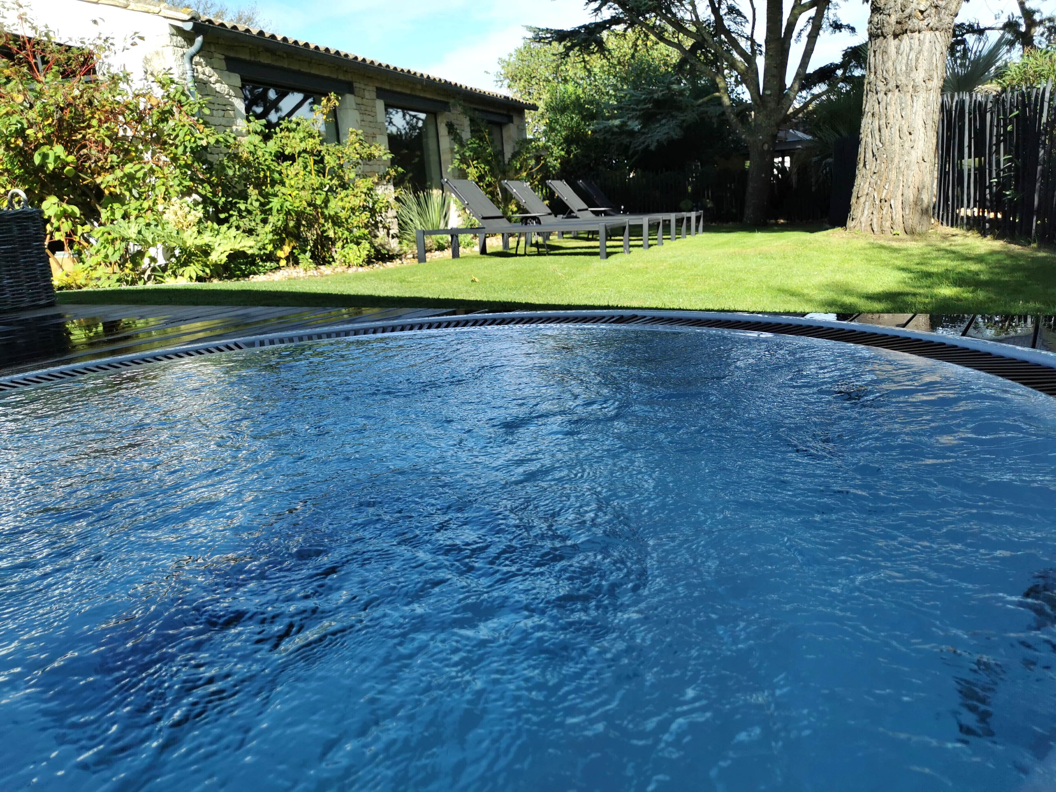 A swimming pool with a stone border, surrounded by a well-maintained lawn and trees.