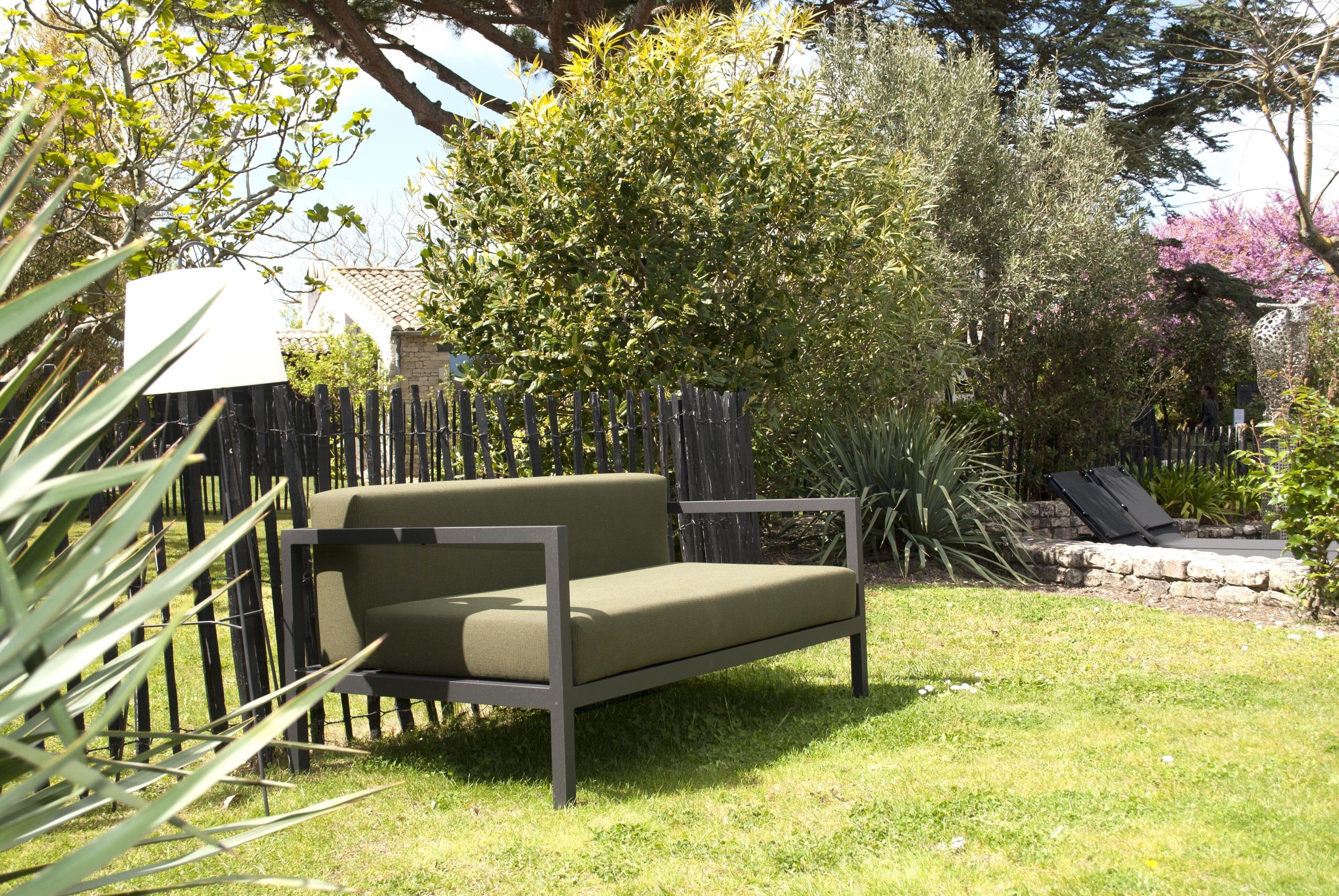 A garden with a green sofa, a wooden fence, and various plants.