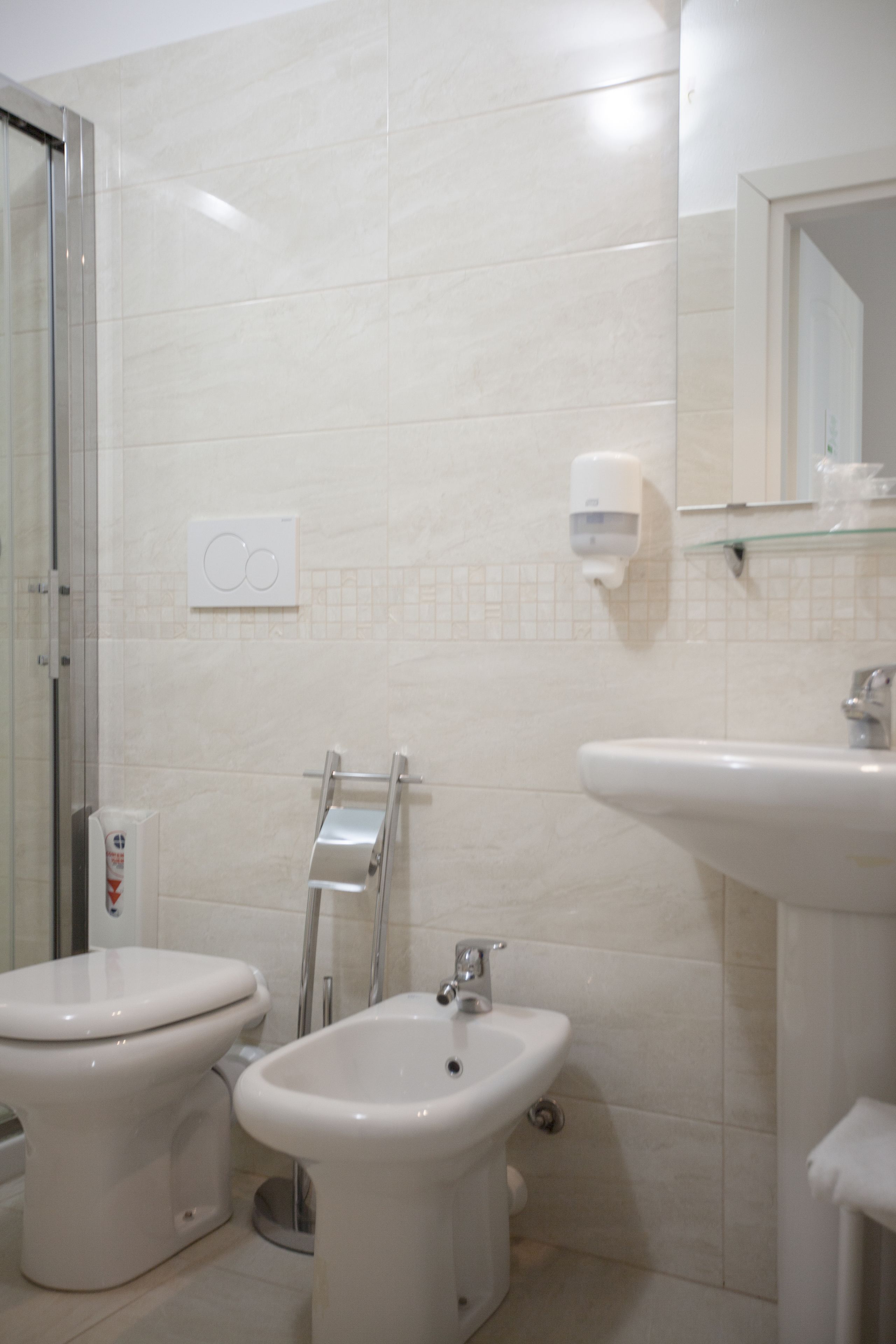 Een badkamer met toilet, bidet, wastafel en een douchecabine van glas.