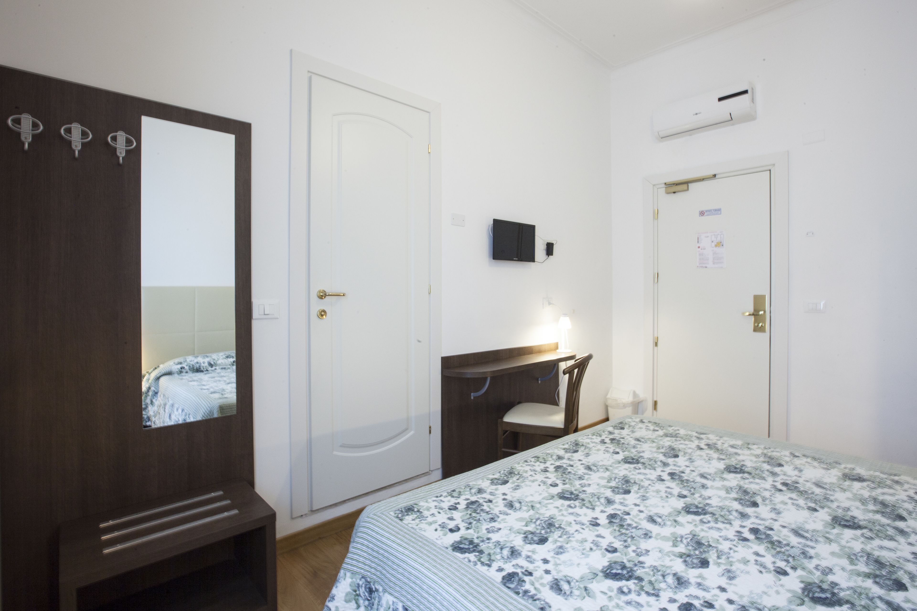 Een slaapkamer met een bed, een dressoir, een spiegel, een bureau met stoel en een televisie.