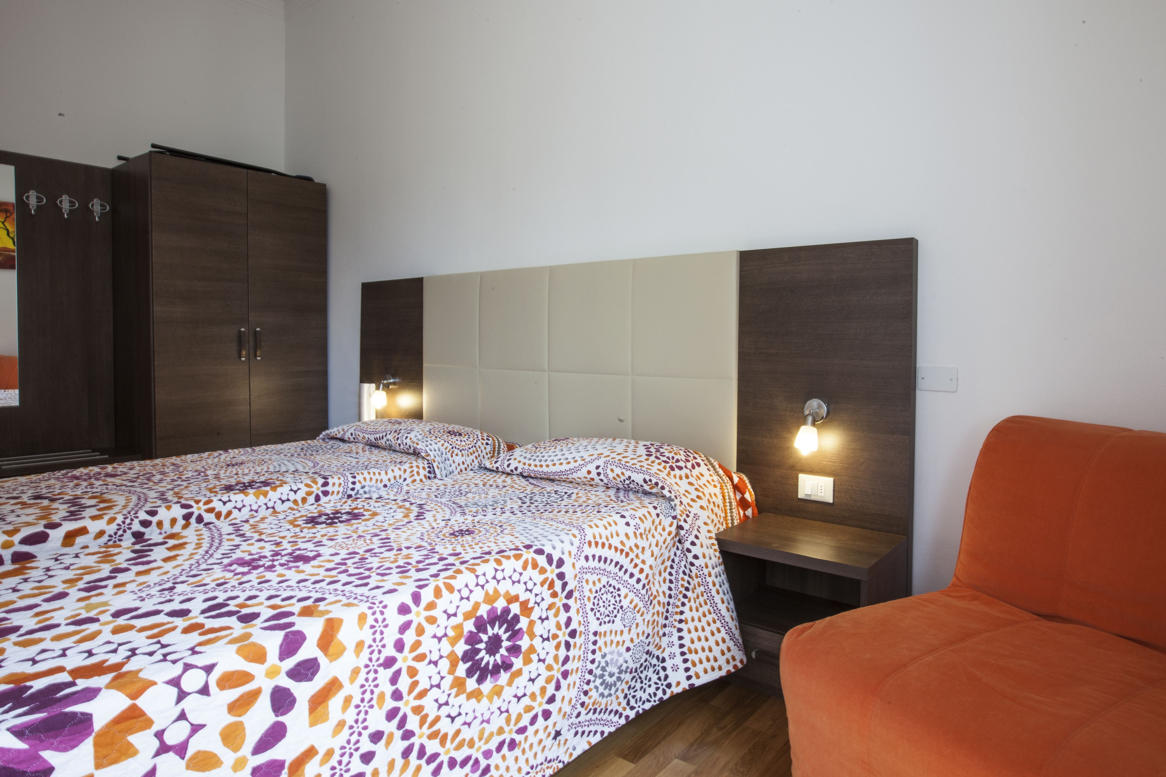 Une chambre à coucher avec un lit, un fauteuil orange, une armoire et deux lampes de chevet.