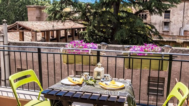 A balcony with a table set for two, two green chairs, a potted plant, and a view of a tree and buildings. - B&B Zen Trastevere (Rome)