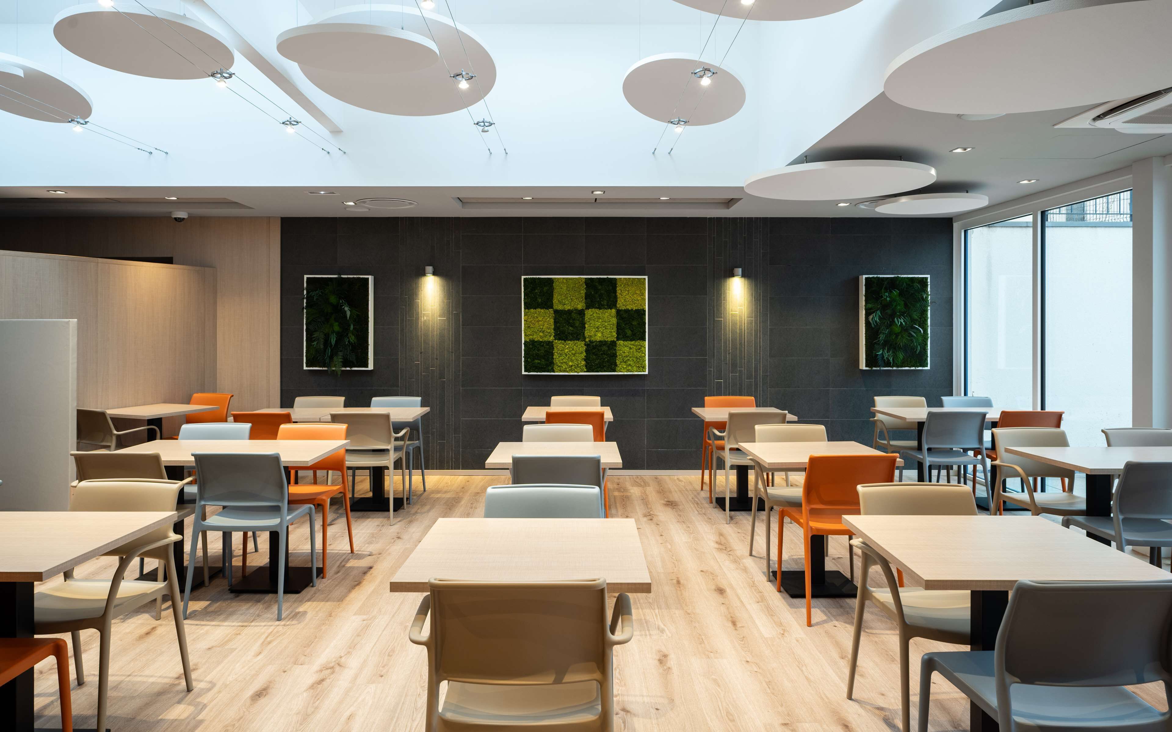 A modern dining area with round tables and chairs, a checkered wall art, and large windows.