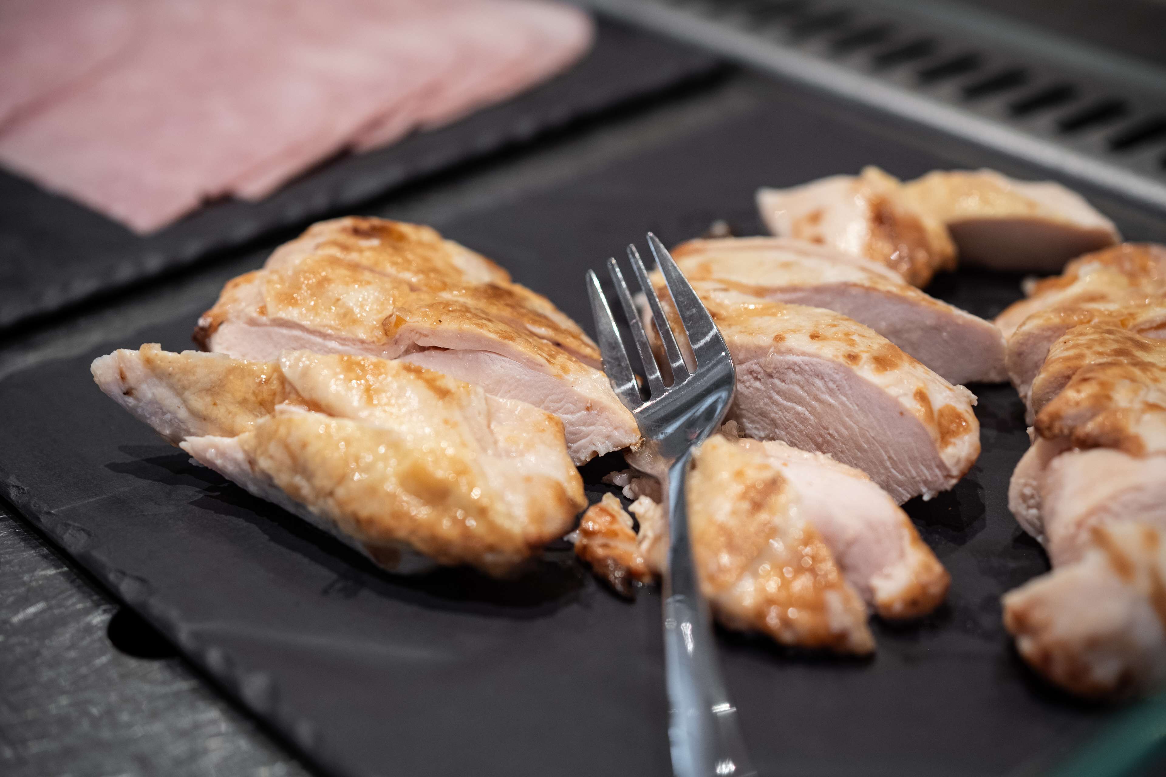 A close-up of sliced cooked chicken on a black plate.
