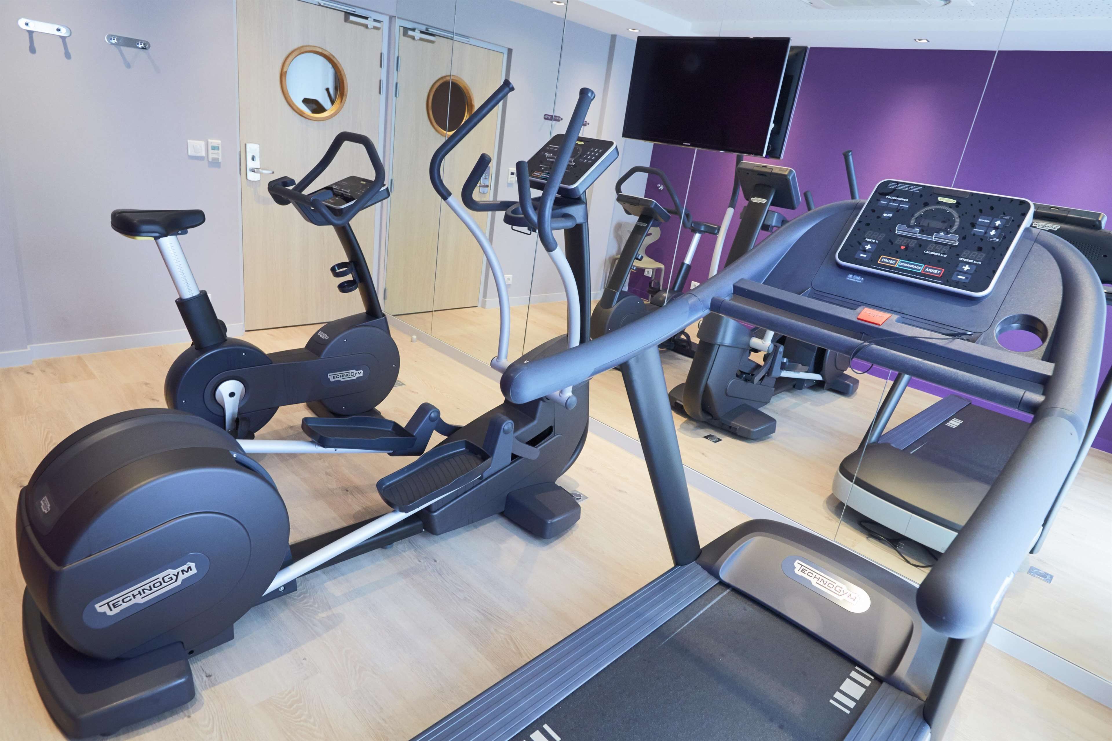 Un gimnasio con varias máquinas de ejercicio, un espejo grande y una televisión.