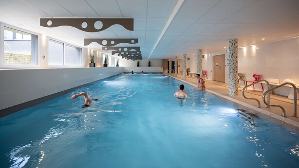 Una piscina interior con agua cristalina, un cartel que indica prohibido bañarse y un cartel que indica prohibido fumar en la pared.