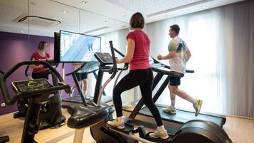 Un gimnasio con cintas de correr, una bicicleta estática y un espejo grande.