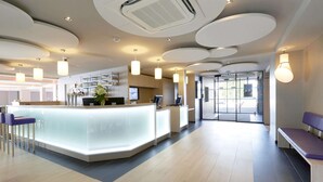 Una moderna zona de recepción con un mostrador central, asientos y un puerta de cristal que da al exterior.