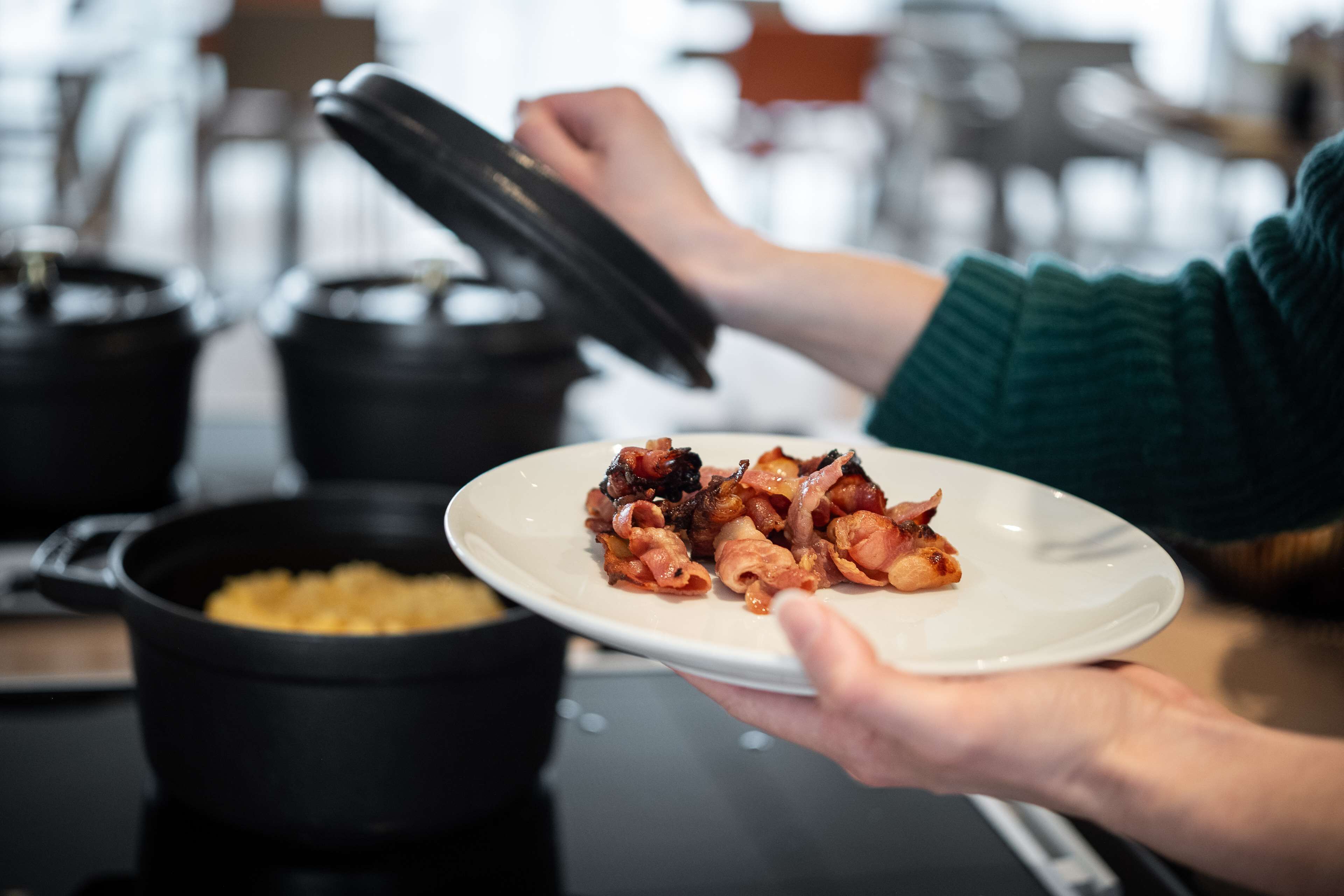 Una persona sosteniendo un plato con comida, una olla sobre la mesa y una cocina al fondo.