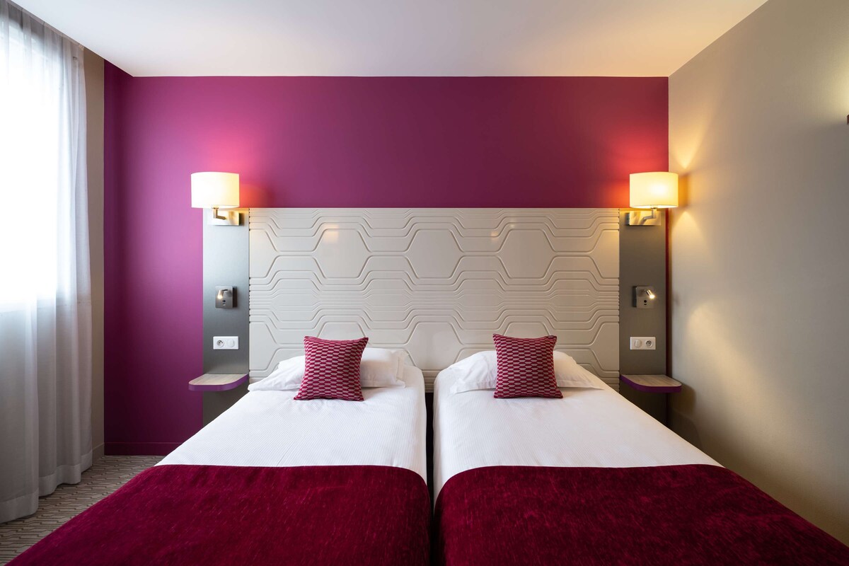 Une chambre d’hôtel avec deux lits, une tête de lit moderne et un éclairage d’ambiance intégré au mur.