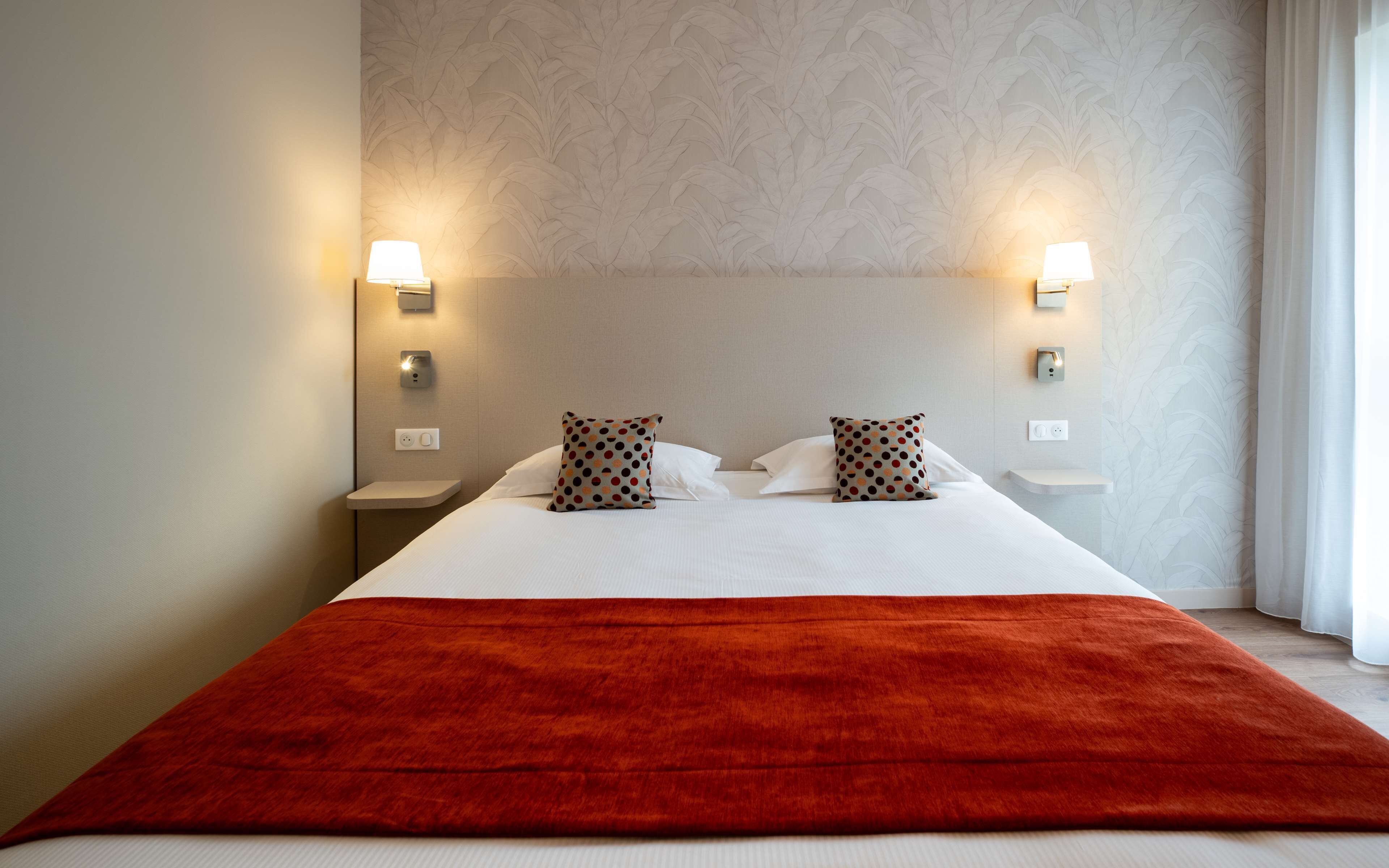 Une chambre d’hôtel avec un grand lit, deux lampes de chevet, une table de chevet et un plaid rouge.