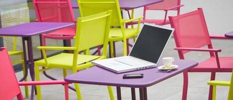 A room with multiple colorful chairs and tables, a laptop on one table, and a cup on another.